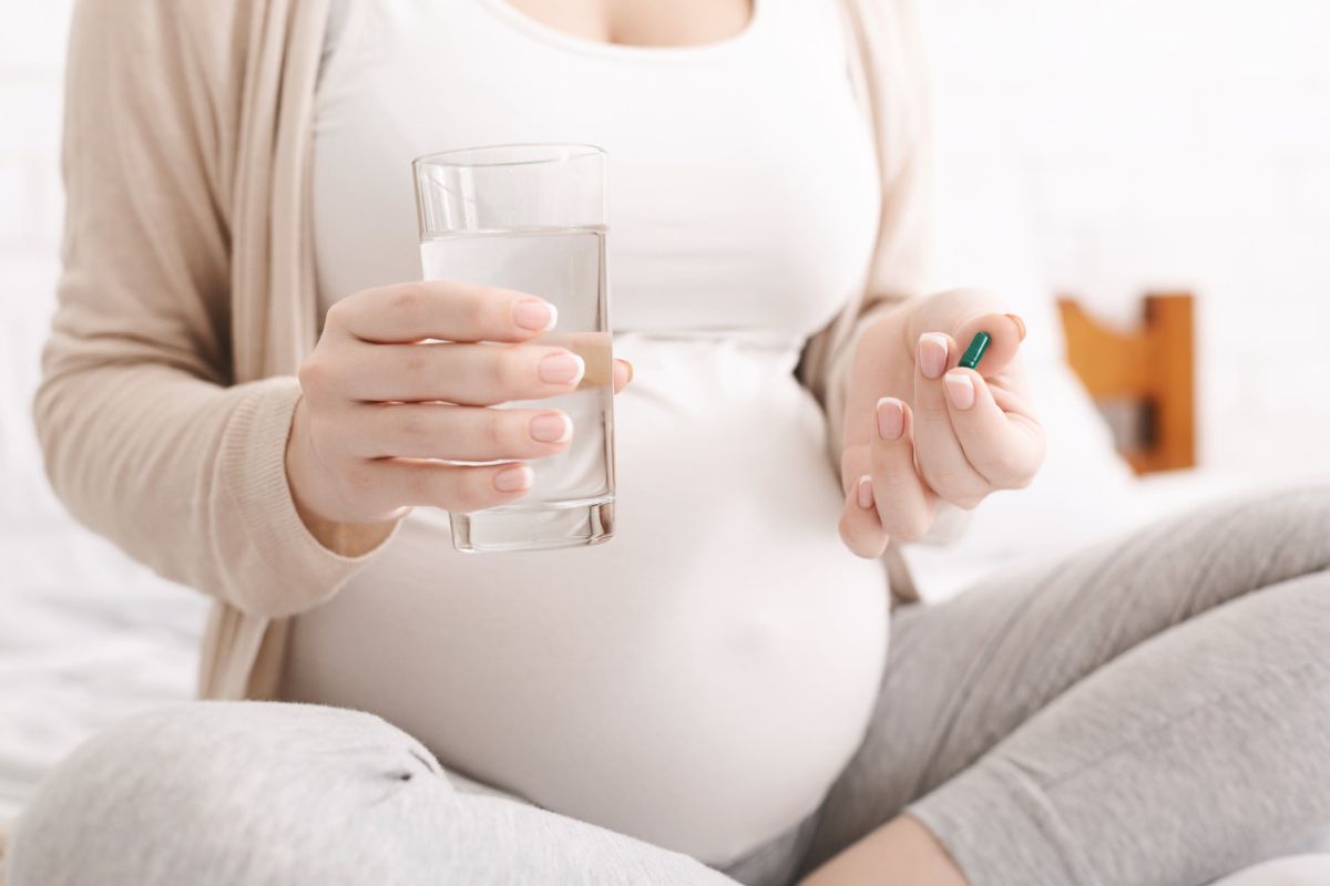 tehotná žena drží pohár s vodou a tabletku
